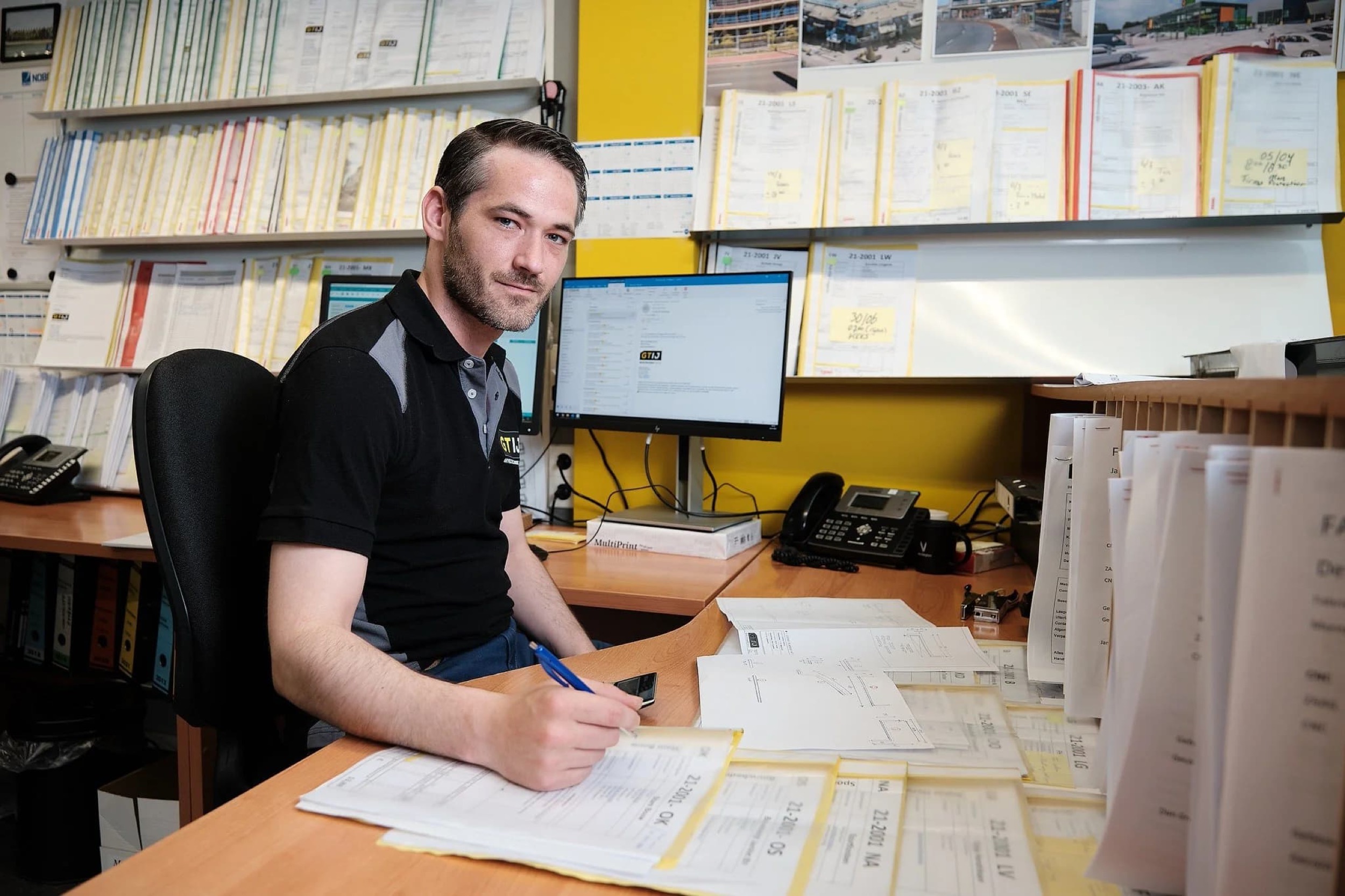 Man aan werkbureau met blauwdrukken, computer en gearchiveerde documenten, professionele kantooromgeving — Stefan Segers Fotografie