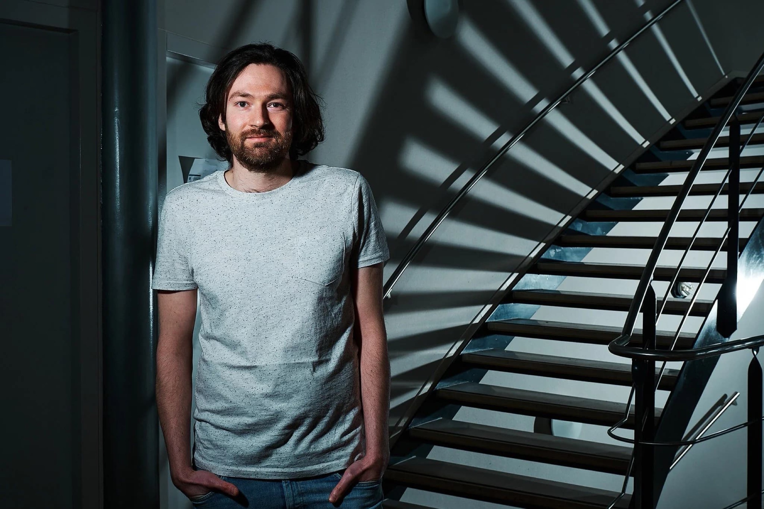 Man in grijs shirt staat bij moderne trap in kantooromgeving, bedrijfsreportage — Stefan Segers Fotografie