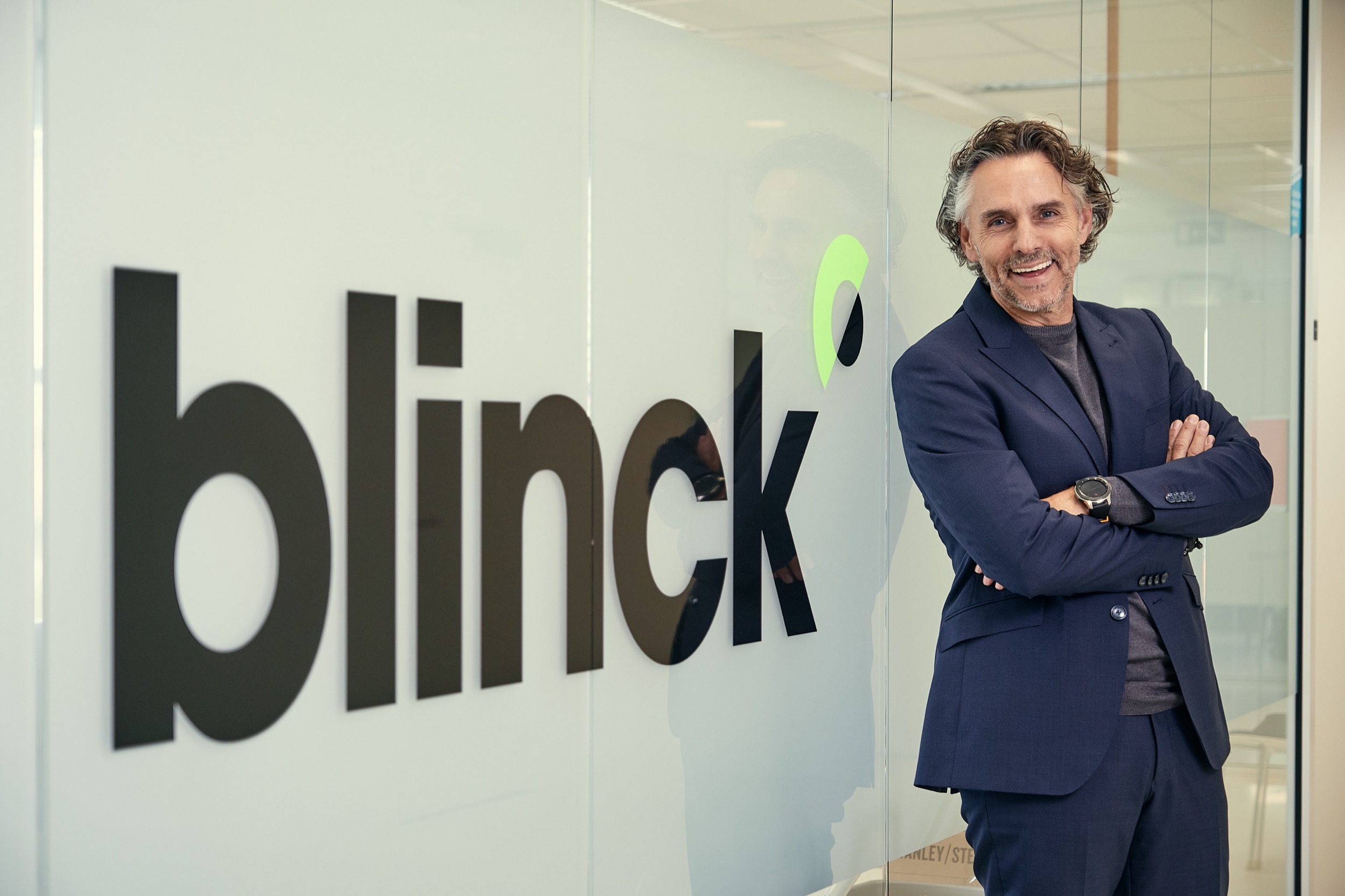 Man in donker pak staat zelfverzekerd voor glazen kantoorwand met Blinck Schoon logo, Almere — Stefan Segers Fotografie