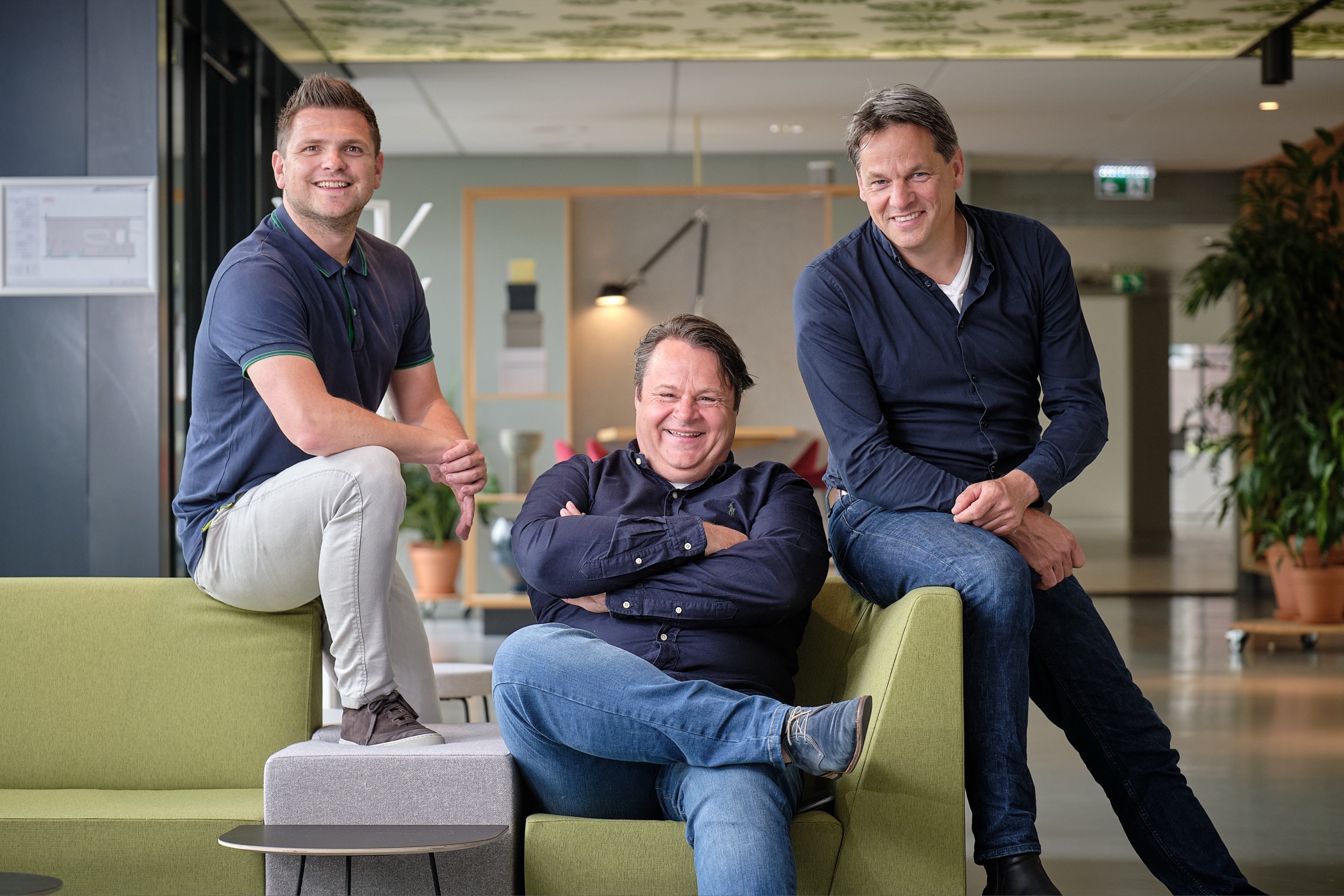 Drie collega's poseren ontspannen op grijsgroene bank in modern kantoor, Nieuwegein — Stefan Segers Fotografie