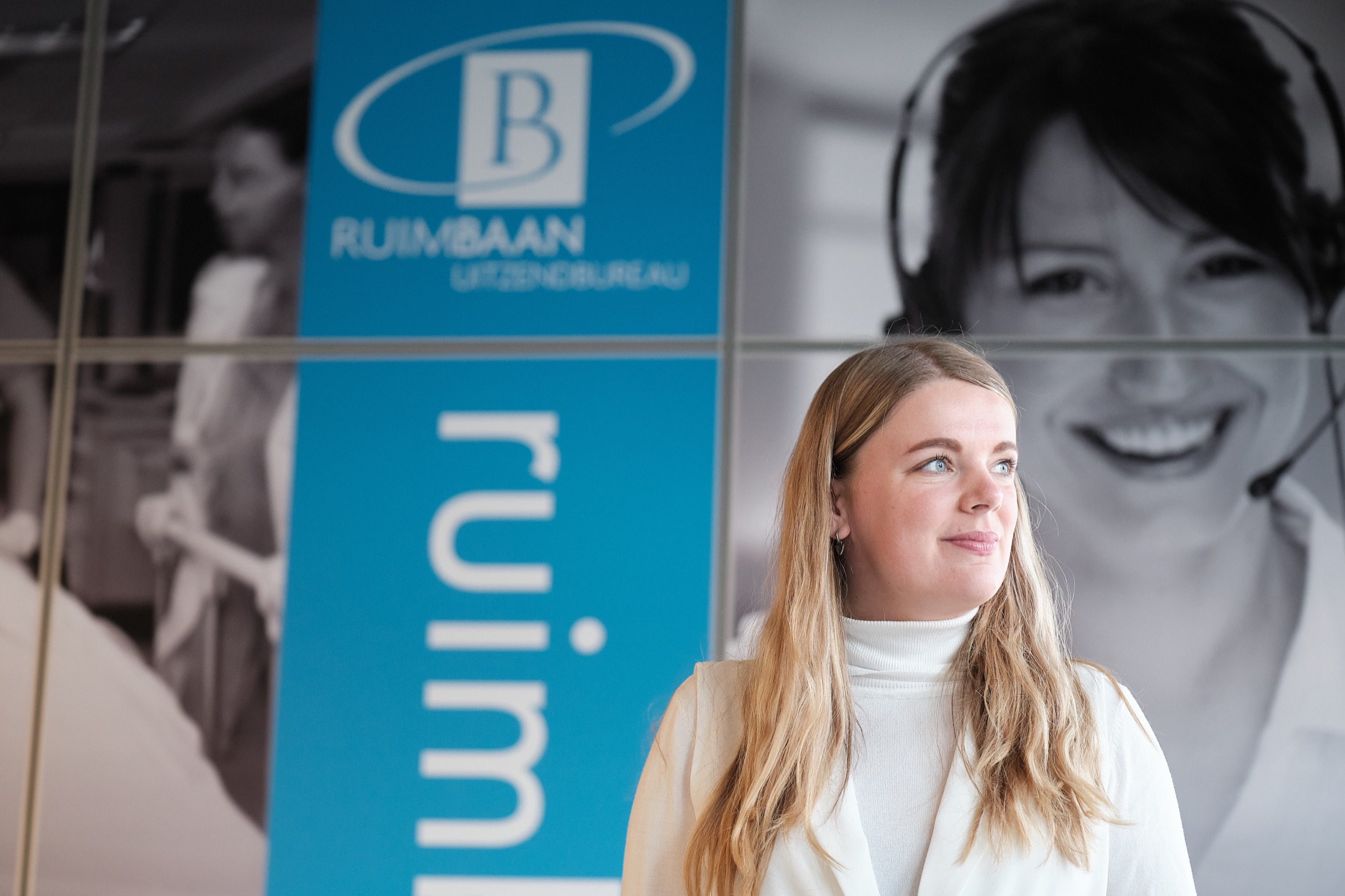 Vrouw in witte coltrui kijkt zijwaarts bij Ruimaan-kantoorbord, professionele bedrijfsreportage — Stefan Segers Fotografie