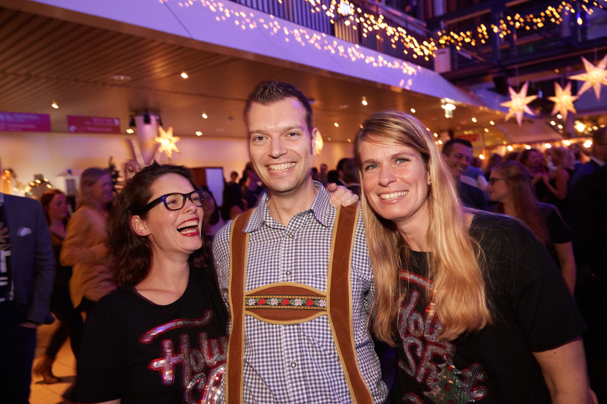 Drie collega's lachen samen op kerstborrel, feestverlichting en sterren op achtergrond, Madurodam Den Haag — Stefan Segers Fotografie