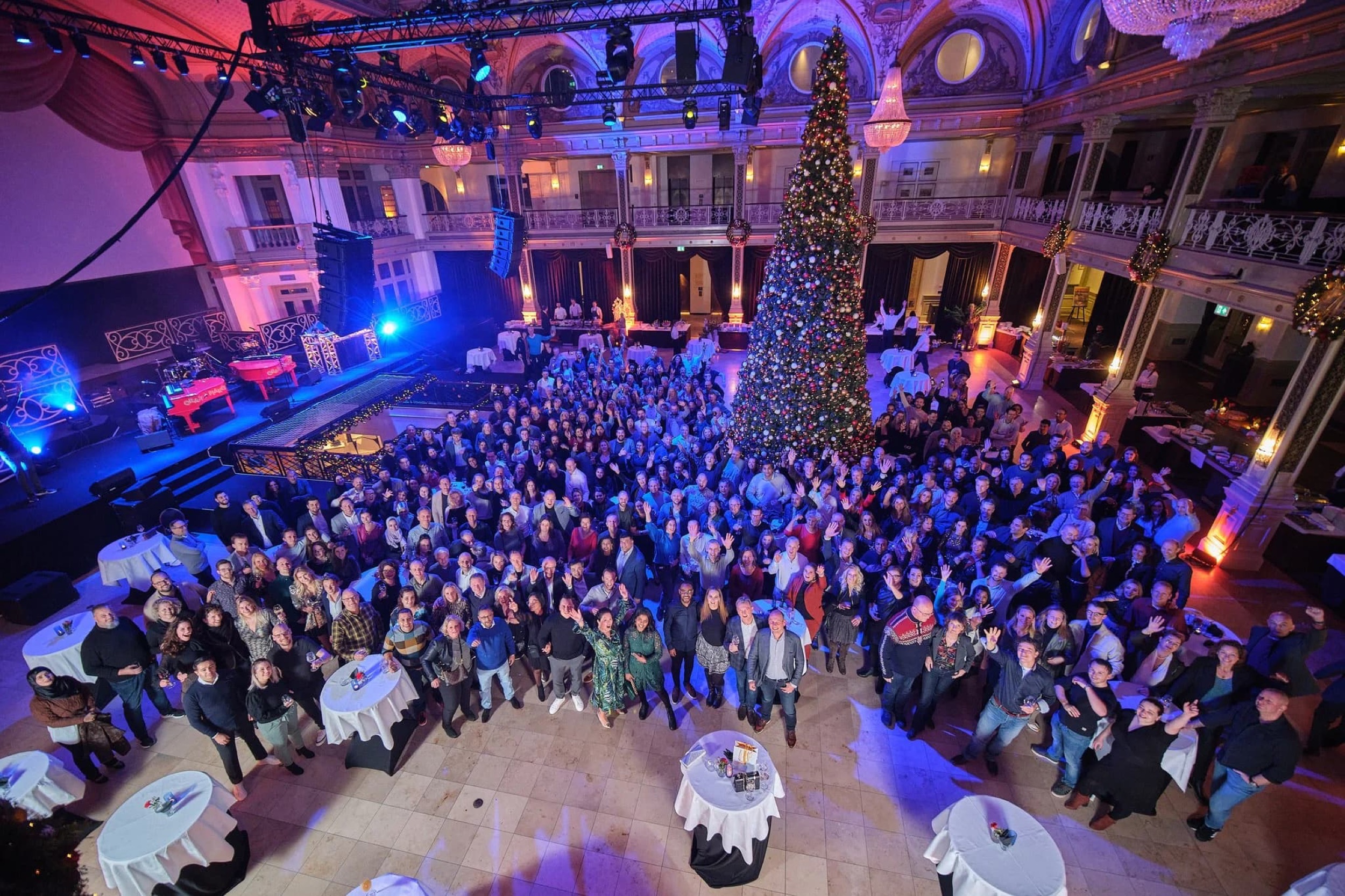 Grote bedrijfsfeest in elegant zalencomplex met honderden gasten, kerstboom en paarse sfeerverlichting — Stefan Segers Fotografie