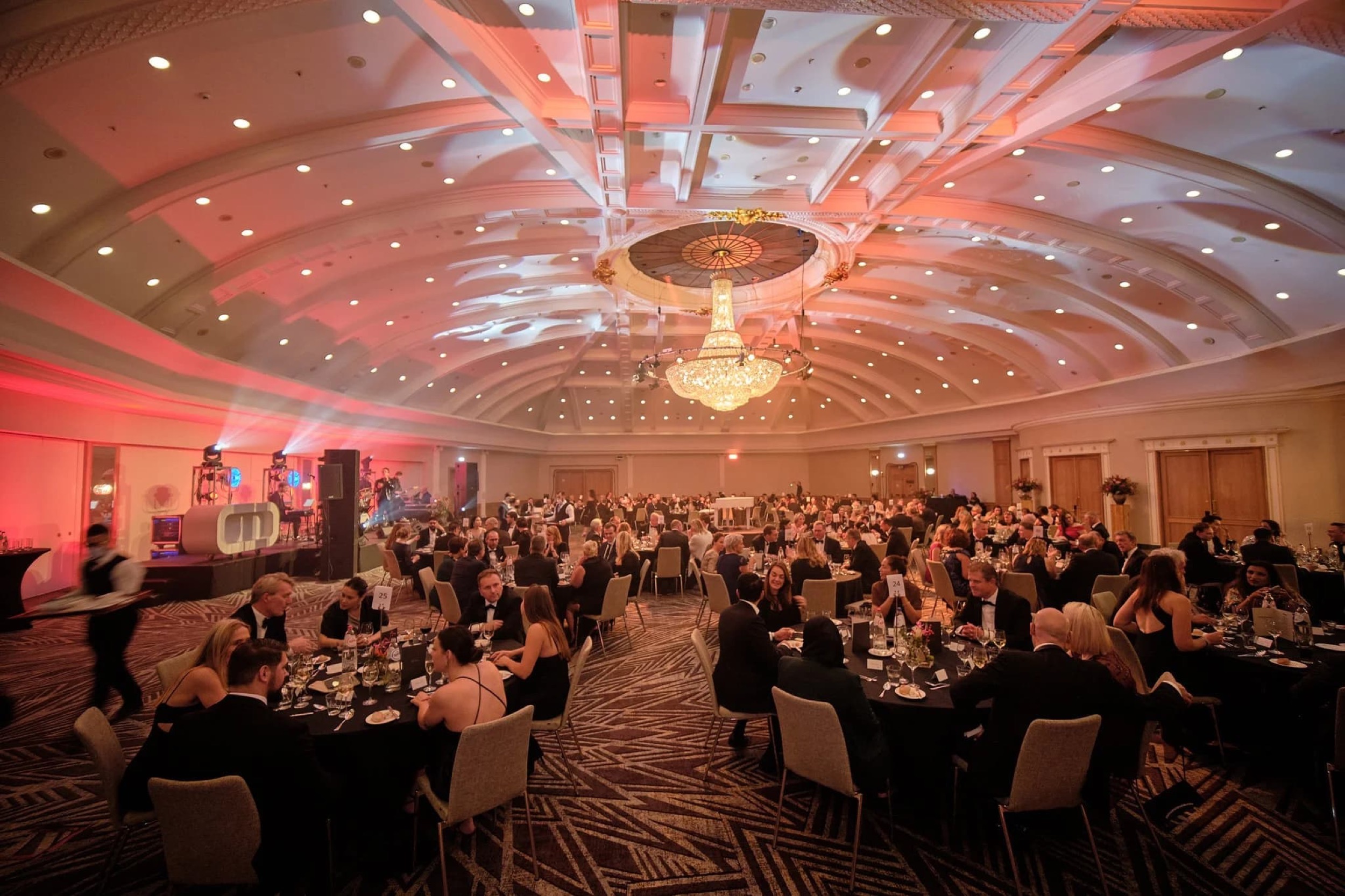 Groot banquetzaal vol gasten aan tafels, roze verlichting, kroonluchter, zakelijk gala — Stefan Segers Fotografie