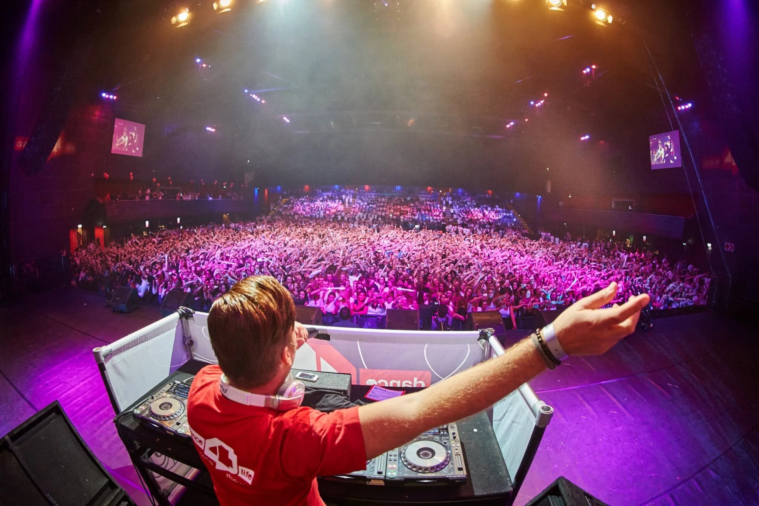 DJ in rood shirt mengt muziek achter decks voor uitgelezen zaal met duizenden bezoekers, paarse verlichting, groot evenement — Stefan Segers Fotografie