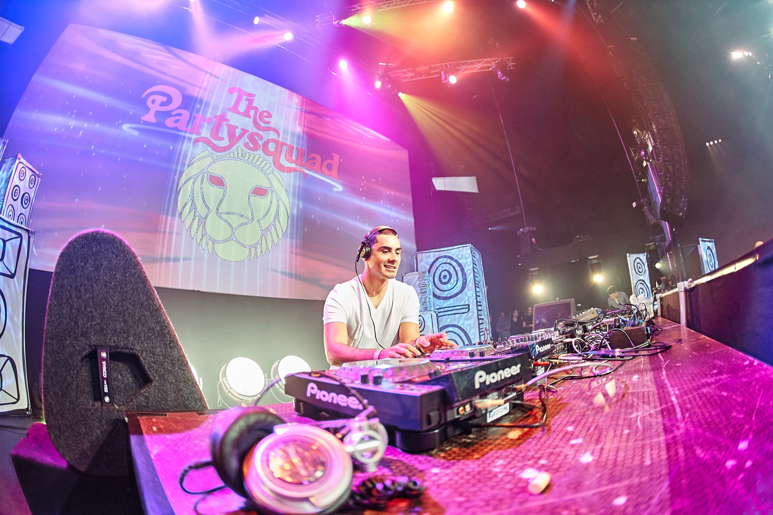 DJ in wit shirt achter Pioneer-deck op podium, kleurrijke verlichting en "The PartySqaud" banner, Heineken Music Hall Amsterdam — Stefan Segers Fotografie