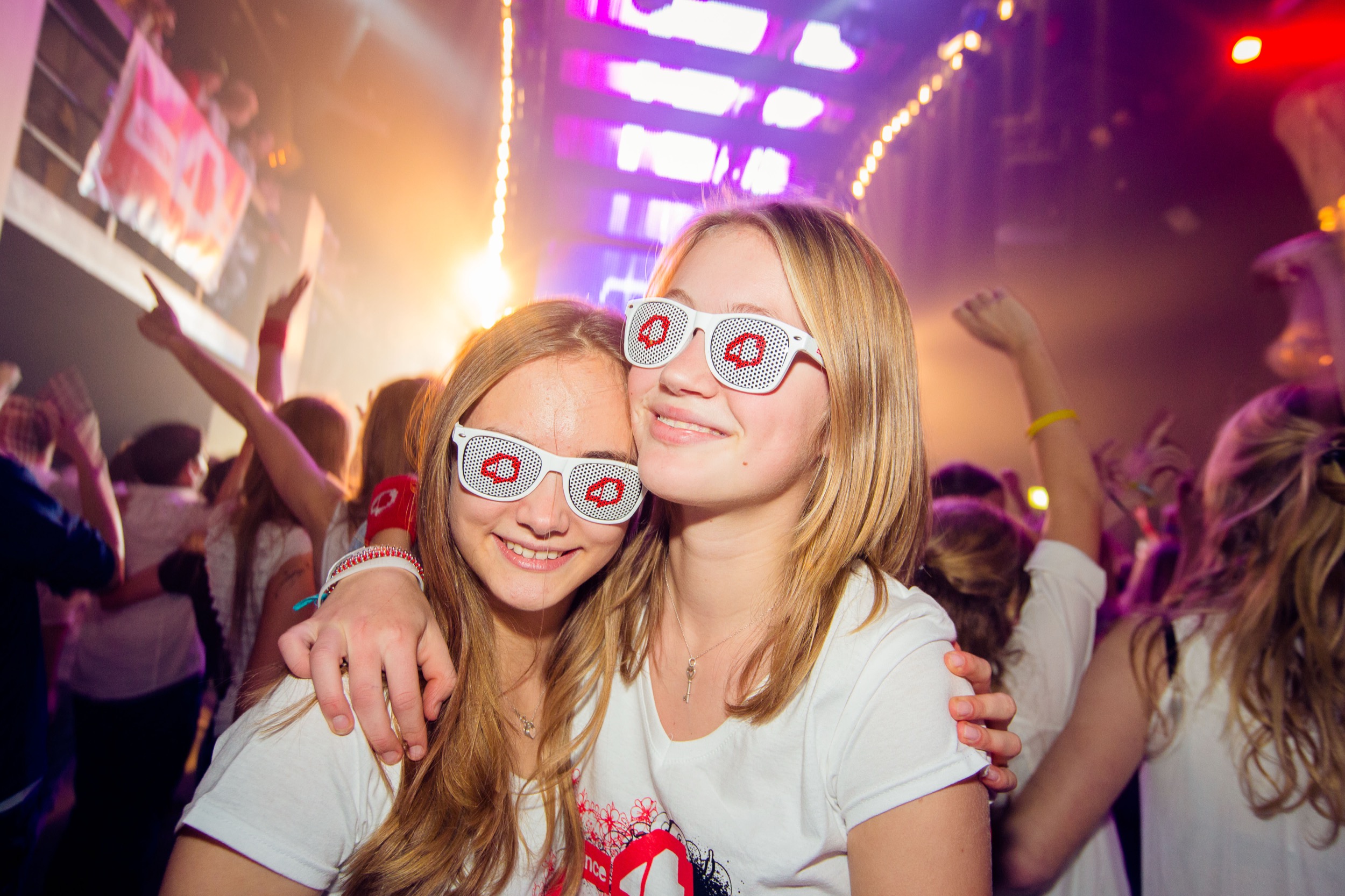 Twee jonge vrouwen in feestoutfits met party-brillen op dansende menigte, Dance 4 Life evenement Bunnik — Stefan Segers Fotografie