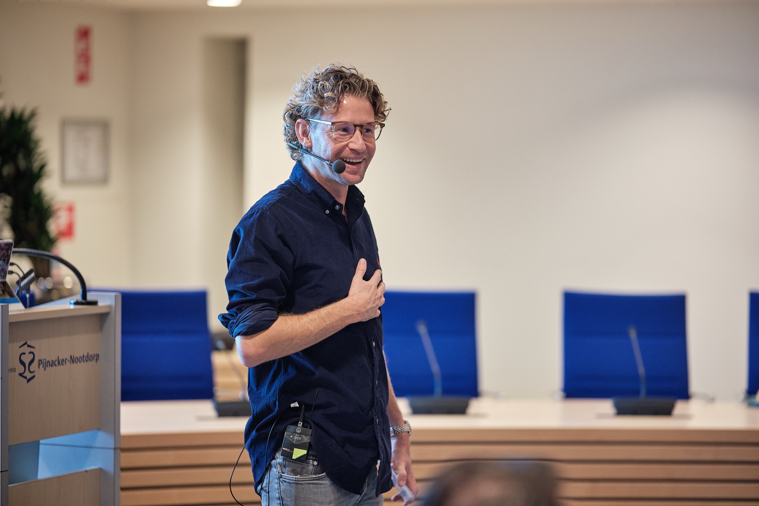 Spreker Ewout Genemans presenteert bij gemeente Pijnacker-Nootdorp, zaal met blauwe stoelen — Stefan Segers Fotografie