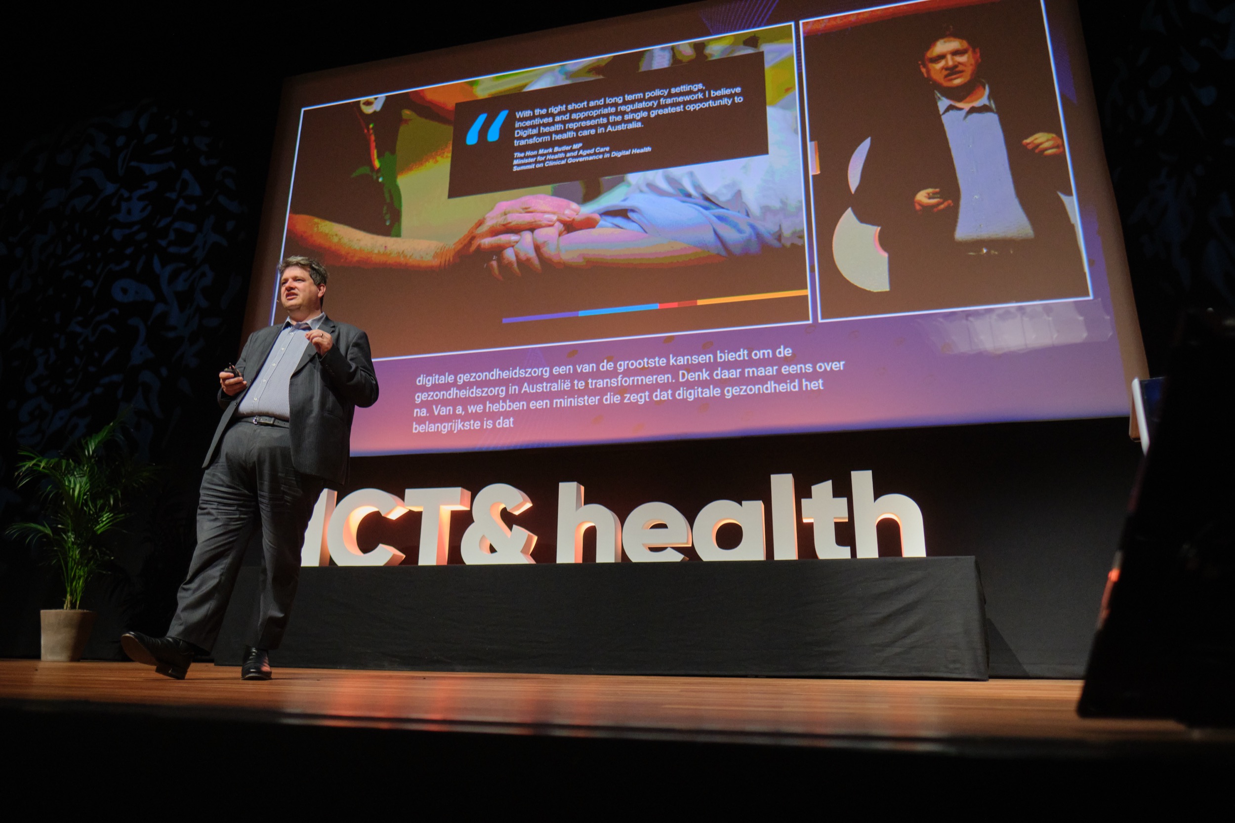 Spreker in donker pak presenteert op podium tijdens ICT&Health congres in MECC Maastricht, grote projectiescherm op achtergrond — Stefan Segers Fotografie