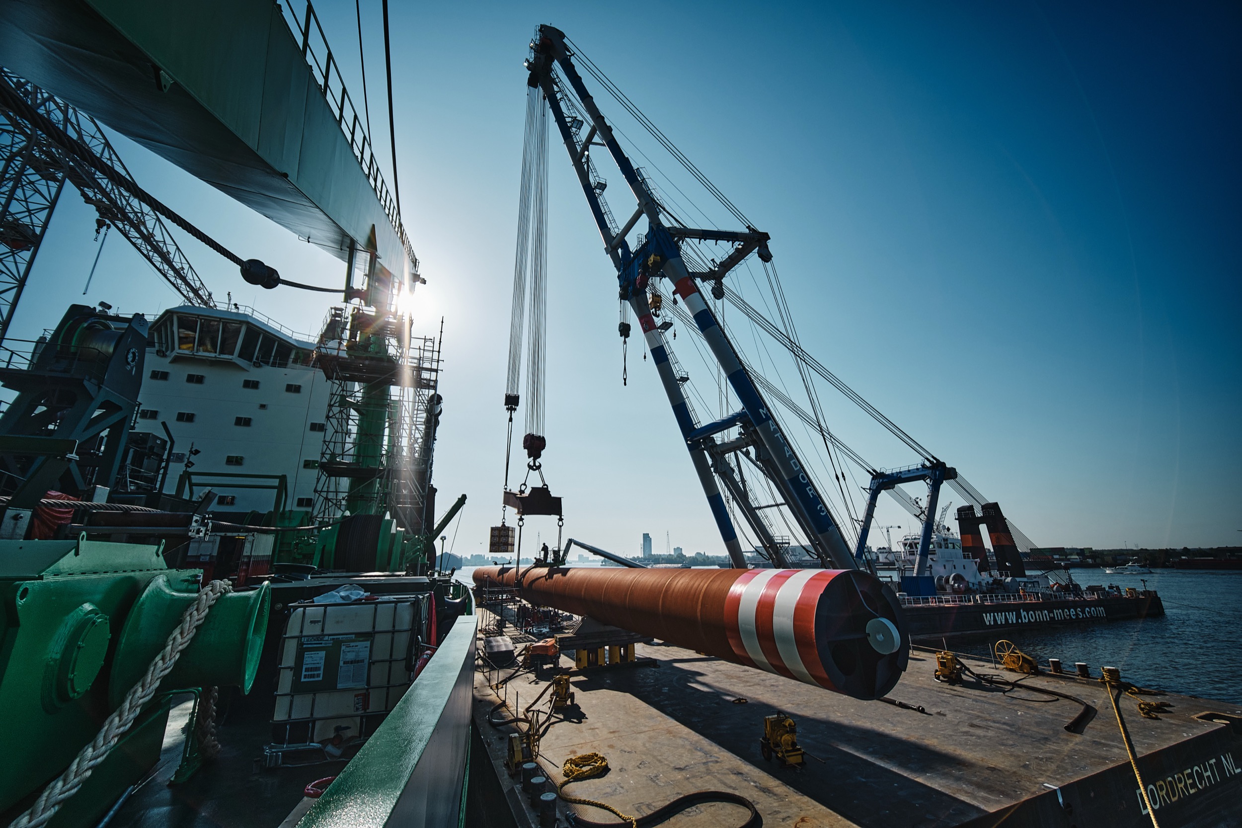 Industriële kraan hijst grote pijp op scheepswerf bij helder weer, zware ladinghanteeringsoperatie — Stefan Segers Fotografie