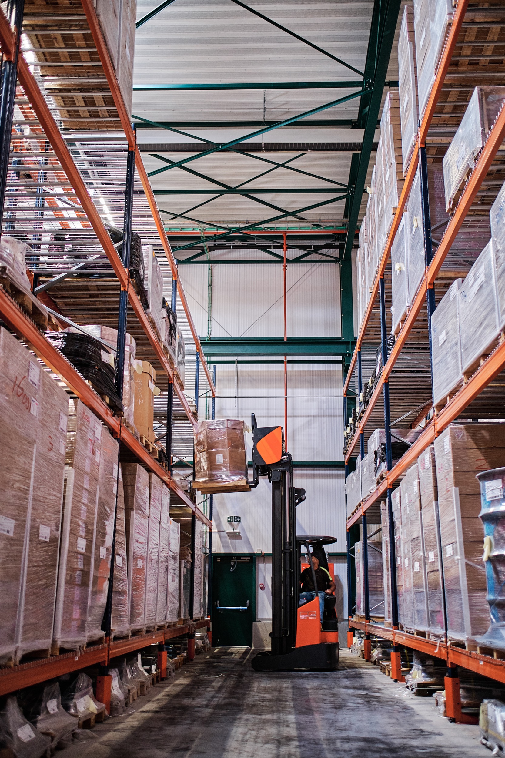 Vorklift met operator in gangpad tussen hoge opslagrijen, industriële magazijnhal, Genk — Stefan Segers Fotografie