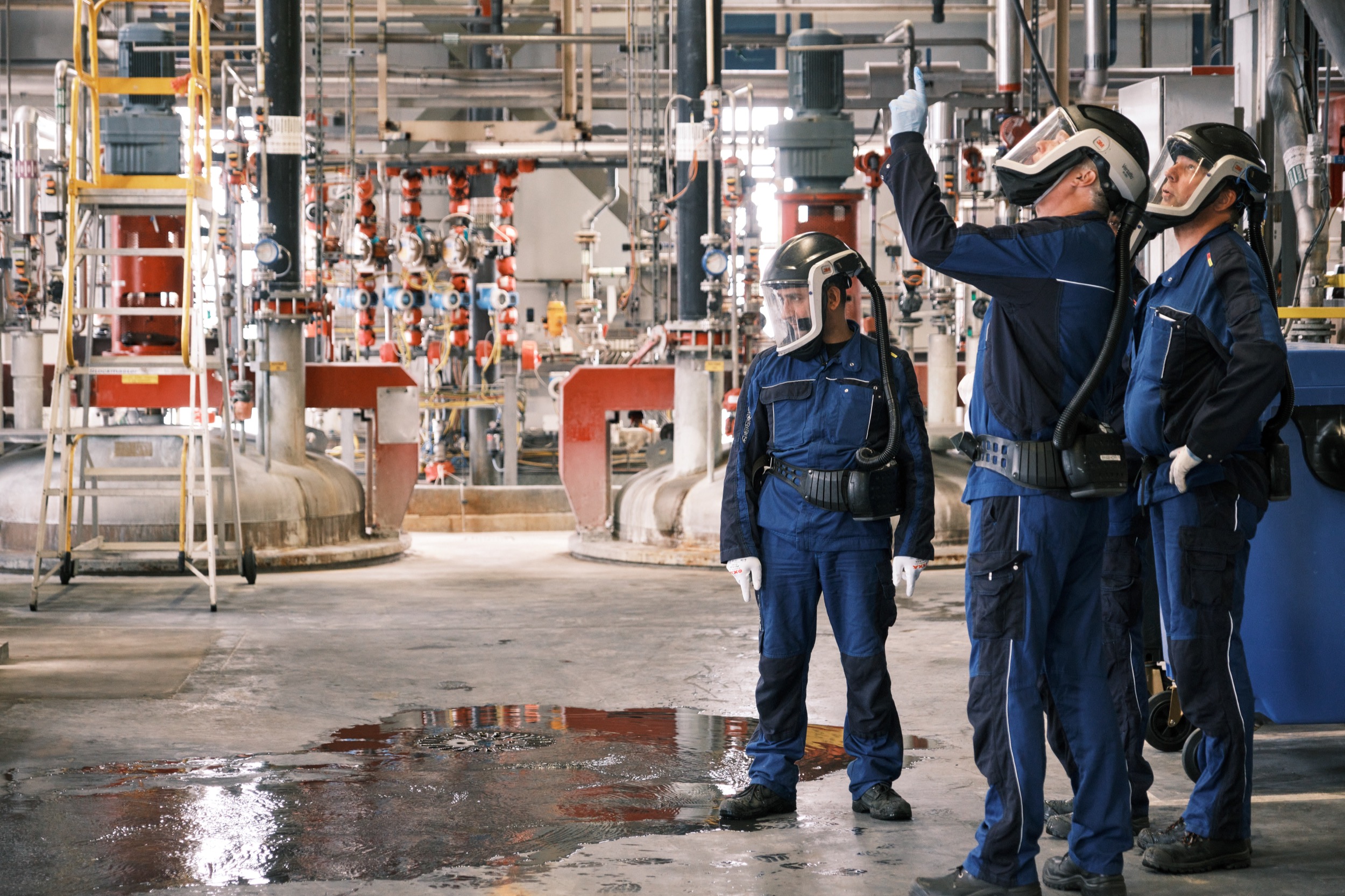 Drie werknemers in blauwe veiligheidsuniform inspecteer complex fabrieksapparatuur, BASF de Meern — Stefan Segers Fotografie