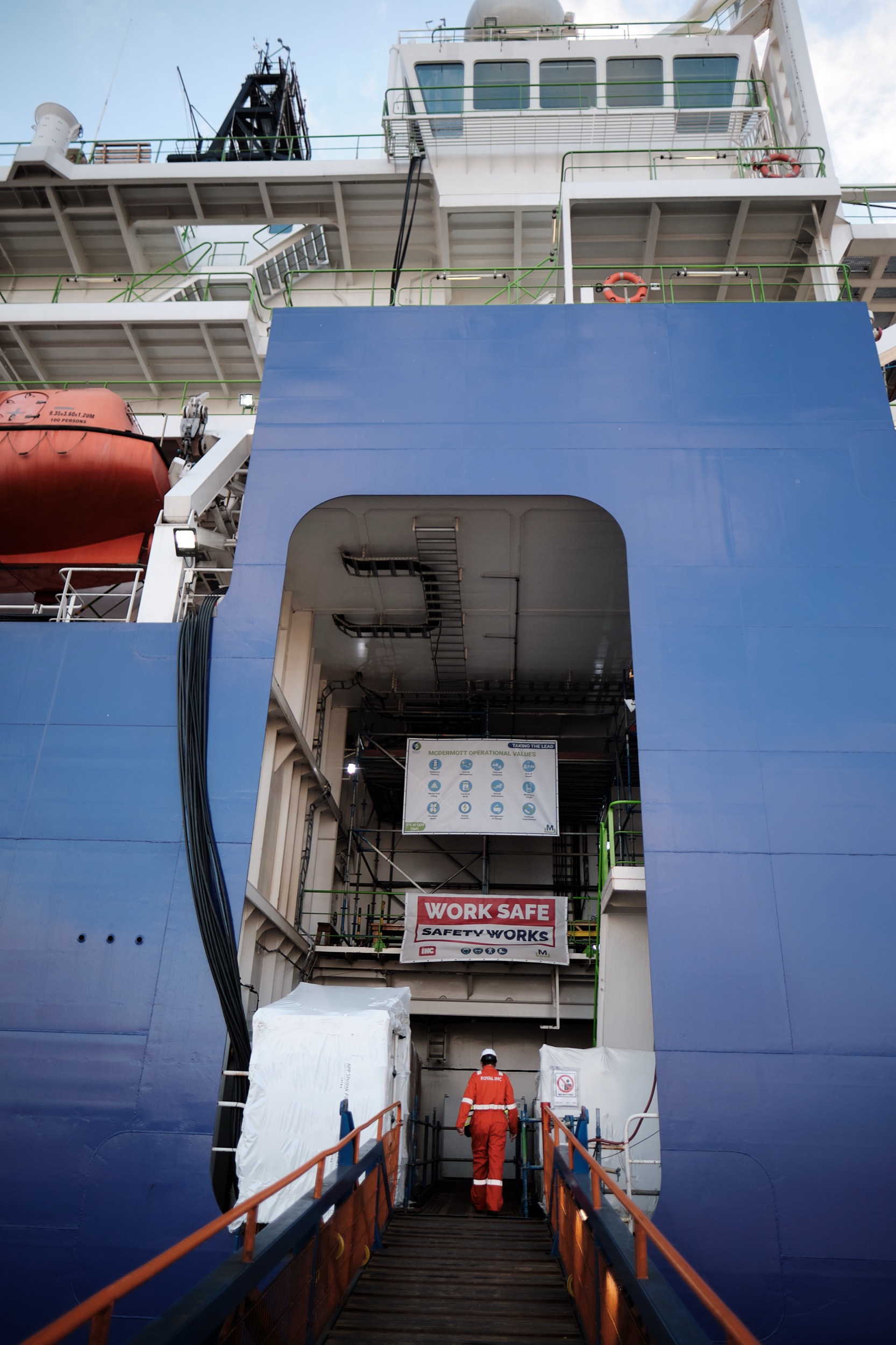 Werknemer in oranje veiligheidskleding op scheepsladder, industrieel scheepsonderhoud Rotterdam — Stefan Segers Fotografie