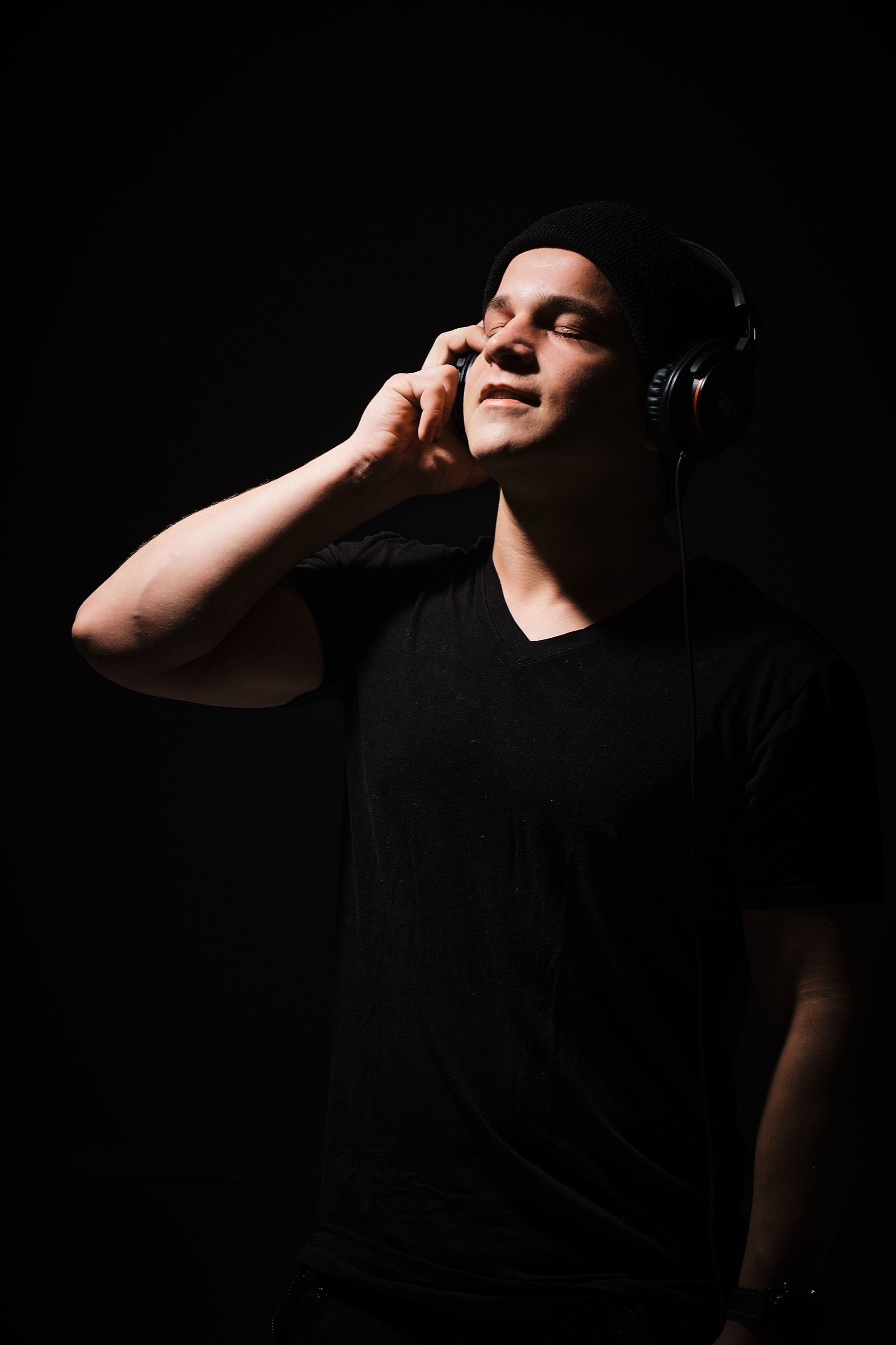 Man met koptelefoon luistert intens naar muziek, zwarte studio-achtergrond, DJ-portretfotografie — Stefan Segers Fotografie