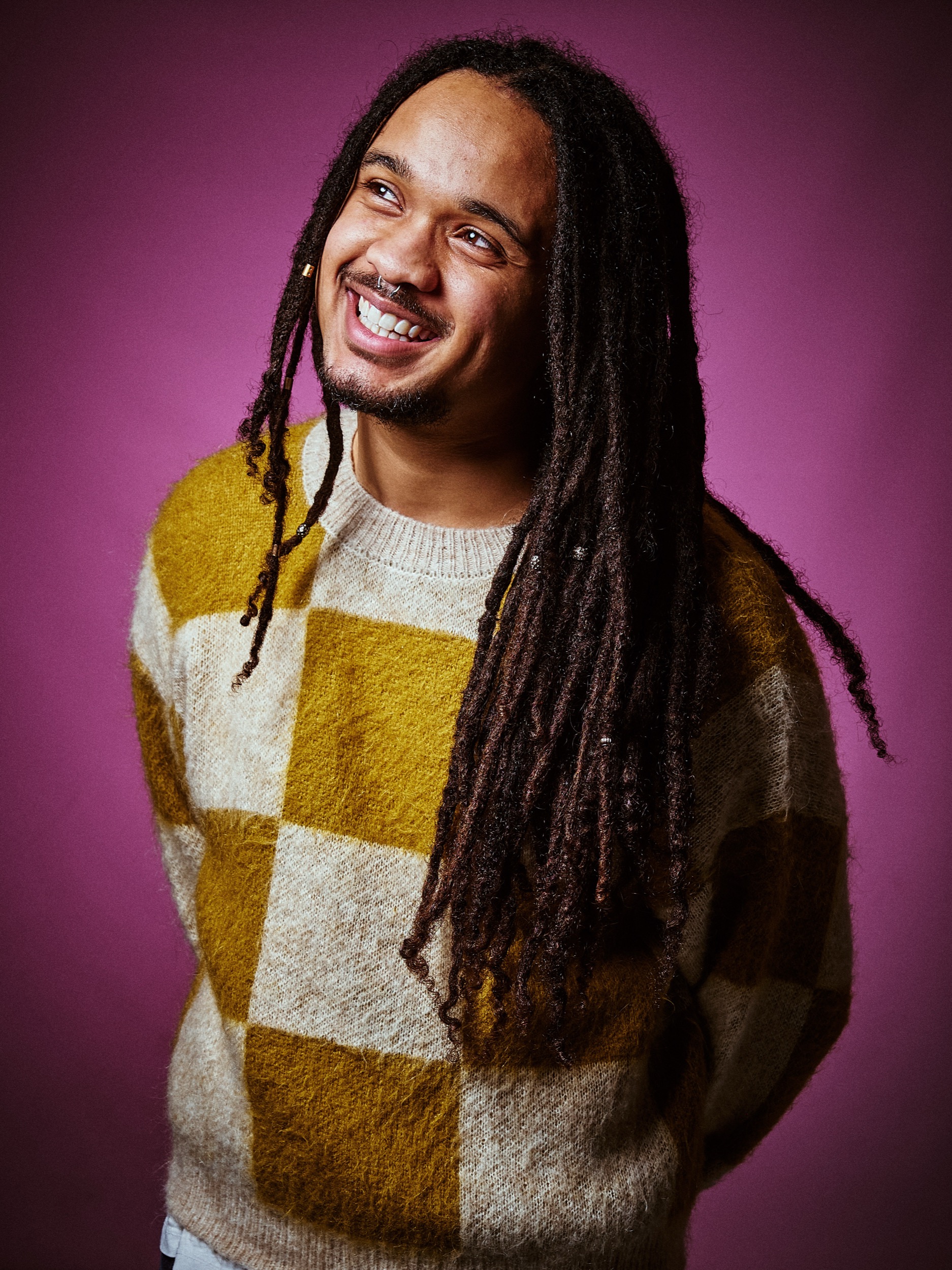 Man met dreadlocks in geel-wit geruit trui lacht naar camera tegen paarse achtergrond, studioportret — Stefan Segers Fotografie