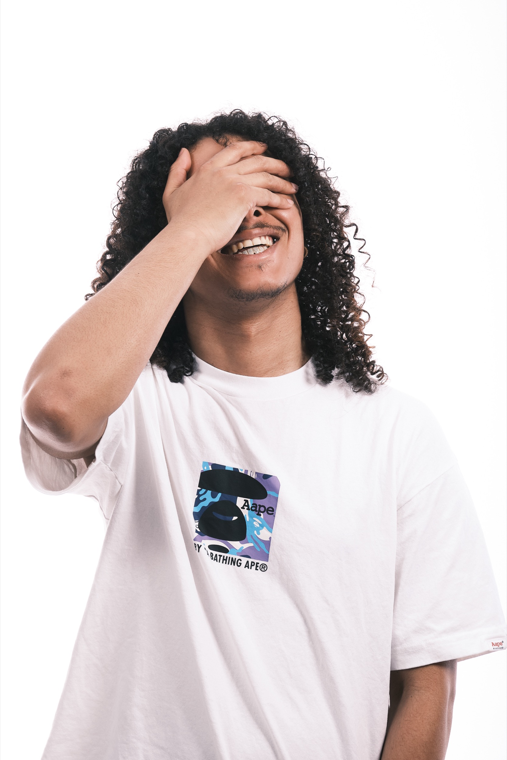 Man met krullend zwart haar lacht uitbundig, hand voor gezicht, witte t-shirt, artistiek portret — Stefan Segers Fotografie