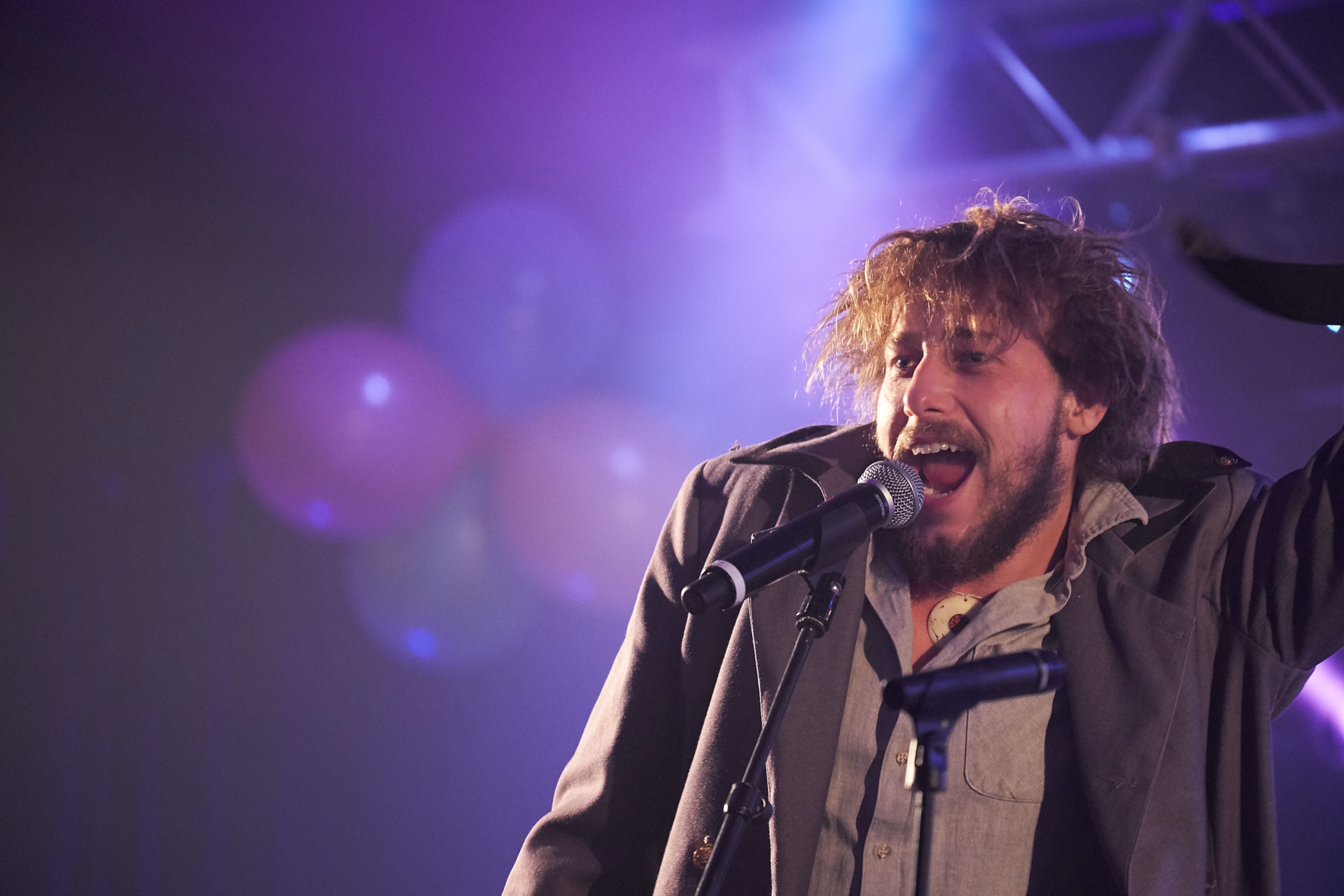 Mannelijke artiest zingt energiek in microfoon op paars verlicht podium, Festival Unlimited Leidschendam — Stefan Segers Fotografie