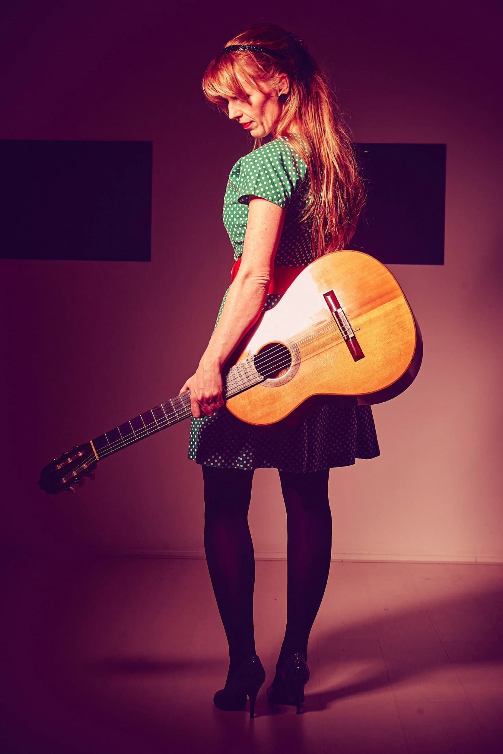 Muziekartiest met akoestische gitaar in groen gebloemde top tegen paarse studioverlichting, professioneel portret — Stefan Segers Fotografie
