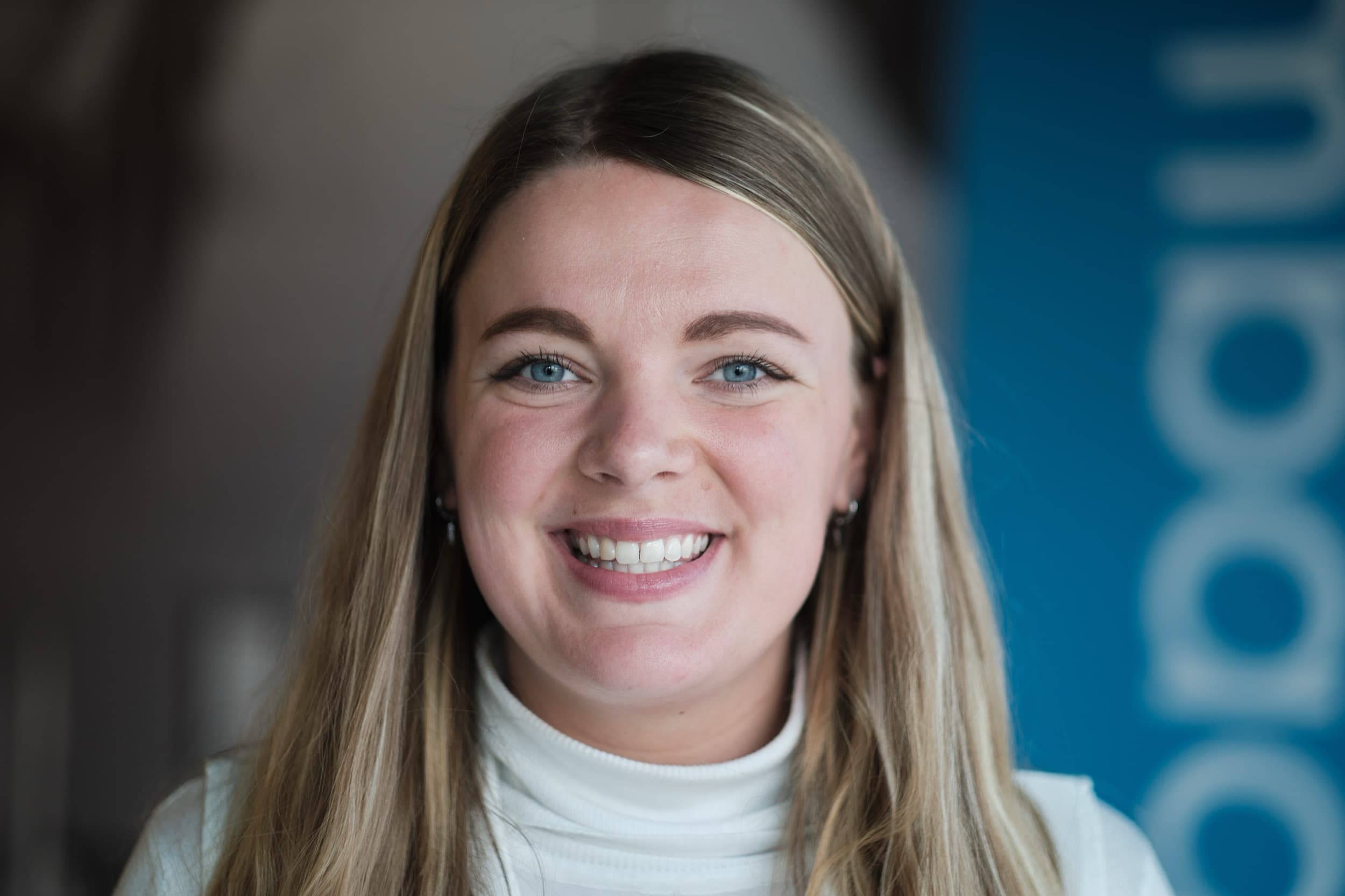 Vrouw met warm glimlach kijkt direct in camera, witte top, blauwe achtergrond, professioneel headshot — Stefan Segers Fotografie