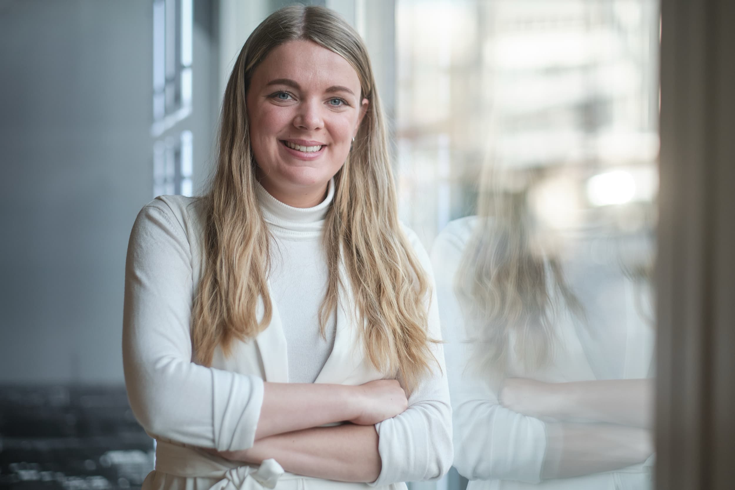 Vrouw in witte trui glimlacht naar camera met gekruiste armen, helder kantoorlicht — Stefan Segers Fotografie