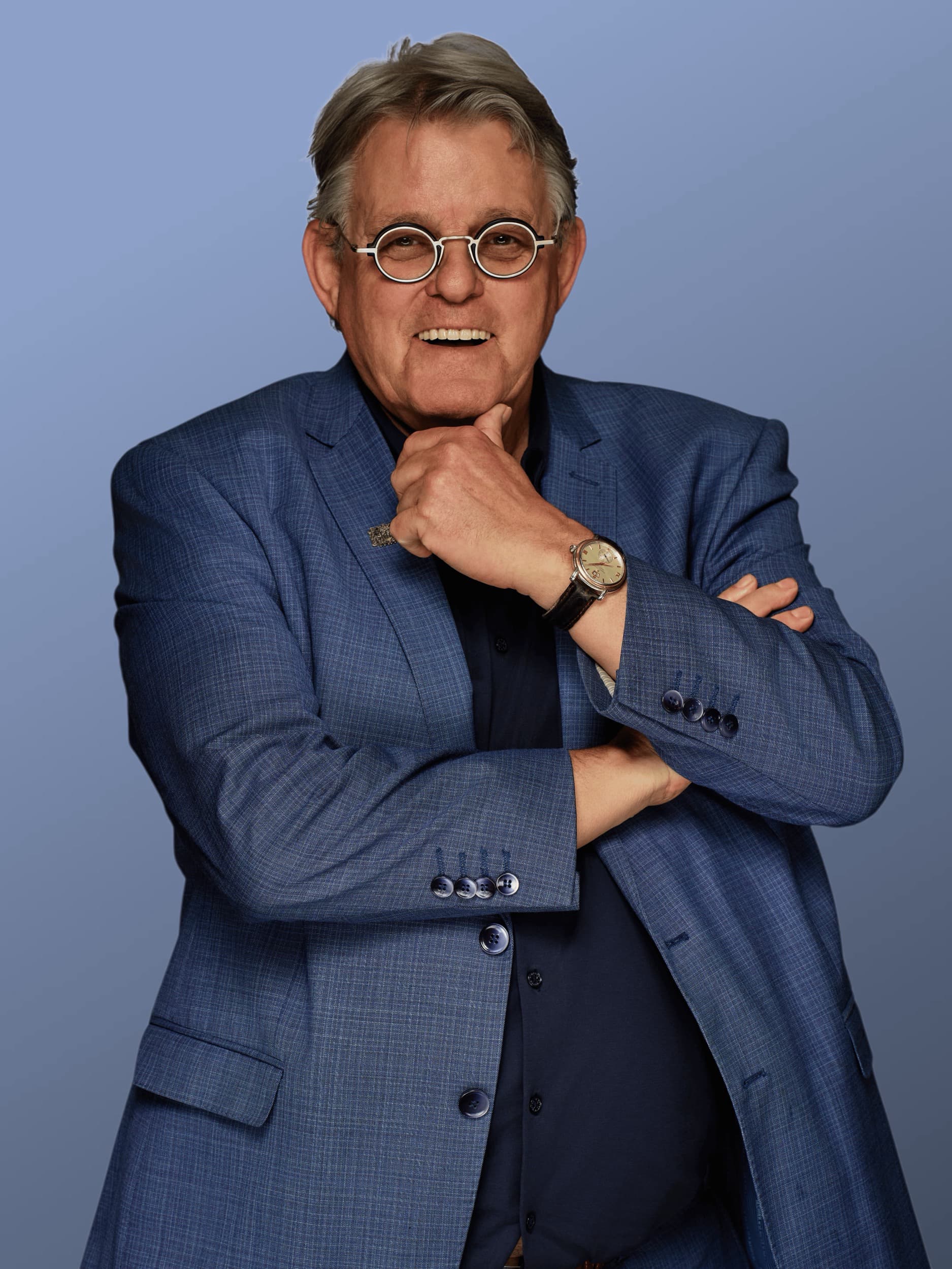 Man in blauw geruit pak met ronde bril, zelfverzekerd portret tegen blauwe achtergrond — Stefan Segers Fotografie