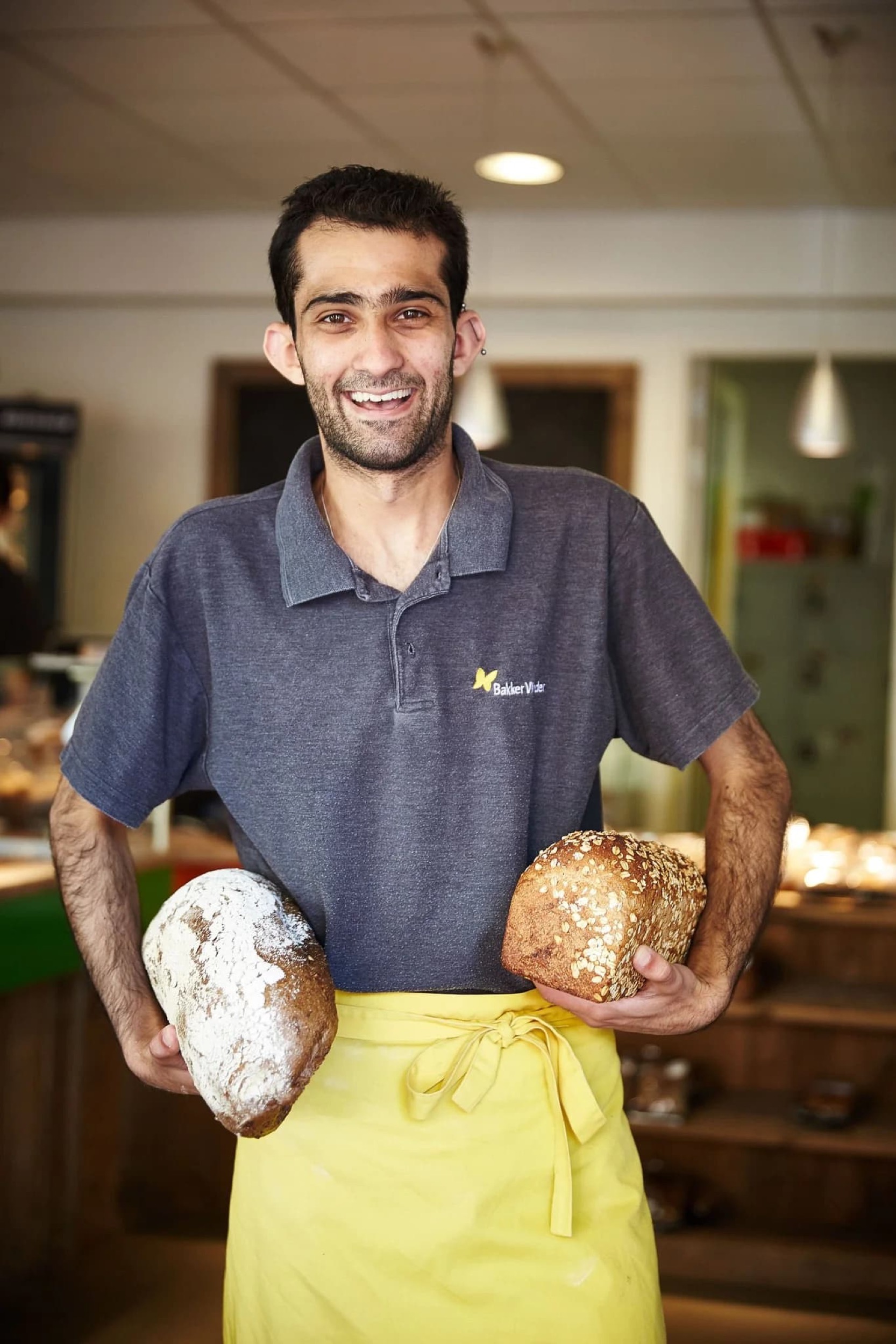 Enthousiaste bakker in bakkerij houdt twee verse broden vast, professionele portretfotografie — Stefan Segers Fotografie