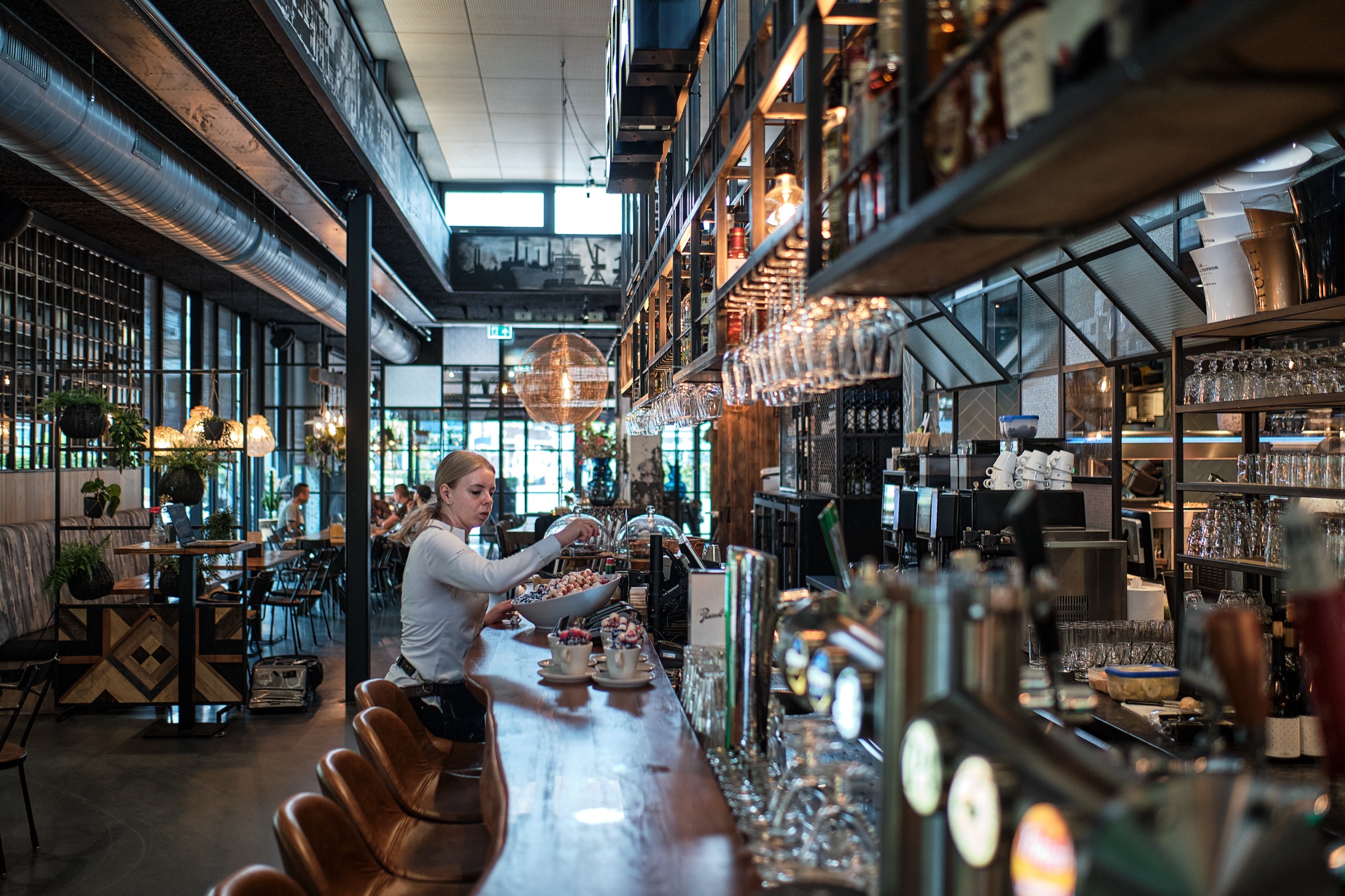 Barista bereidt drankje achter bar in modern horecagebouw, BenN-groep Beverwijk, sfeervolle architectuur — Stefan Segers Fotografie