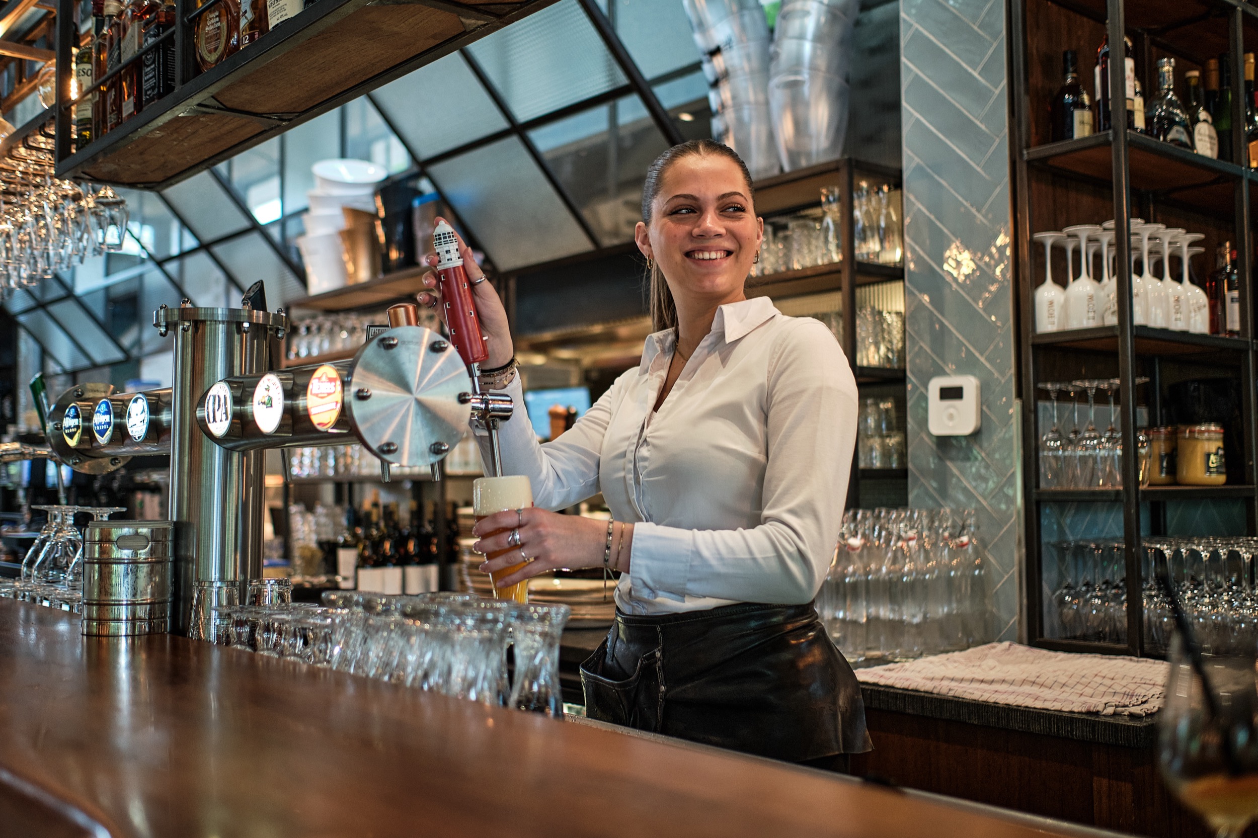 Barista glimlacht terwijl ze drankje schenkt aan bar, moderne horeca-omgeving Beverwijk — Stefan Segers Fotografie